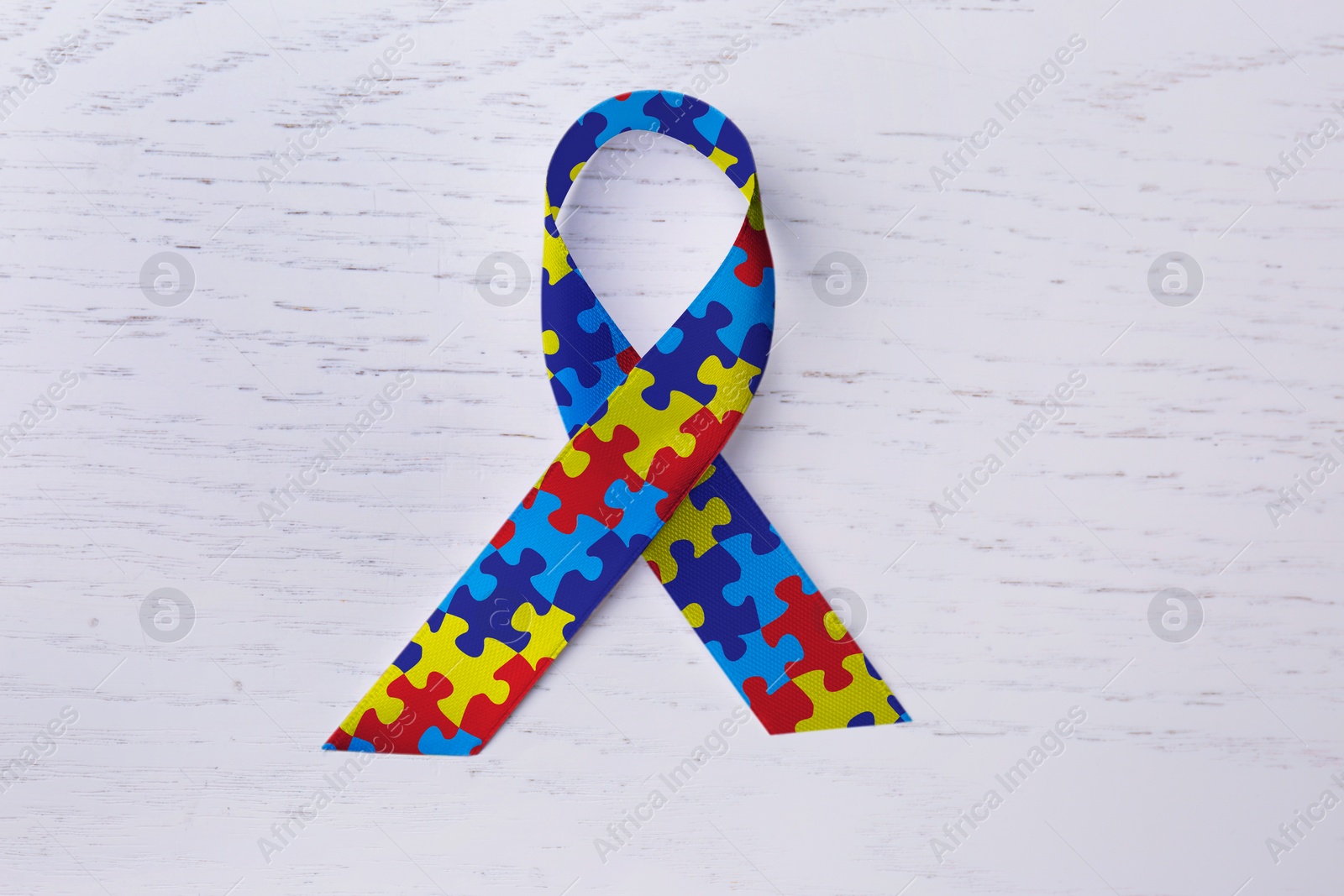 Image of World Autism Awareness Day. Colorful puzzle ribbon on white wooden background, top view