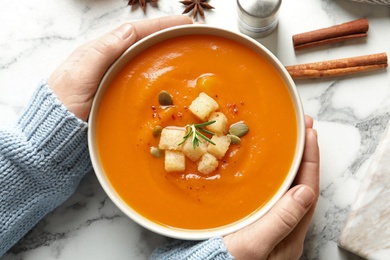 Photo of Woman with bowl of tasty sweet potato soup at table, top view