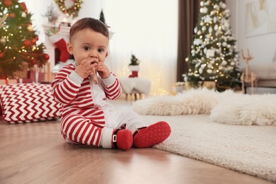 Photo of Cute baby wearing bright pajamas on floor in room decorated for Christmas