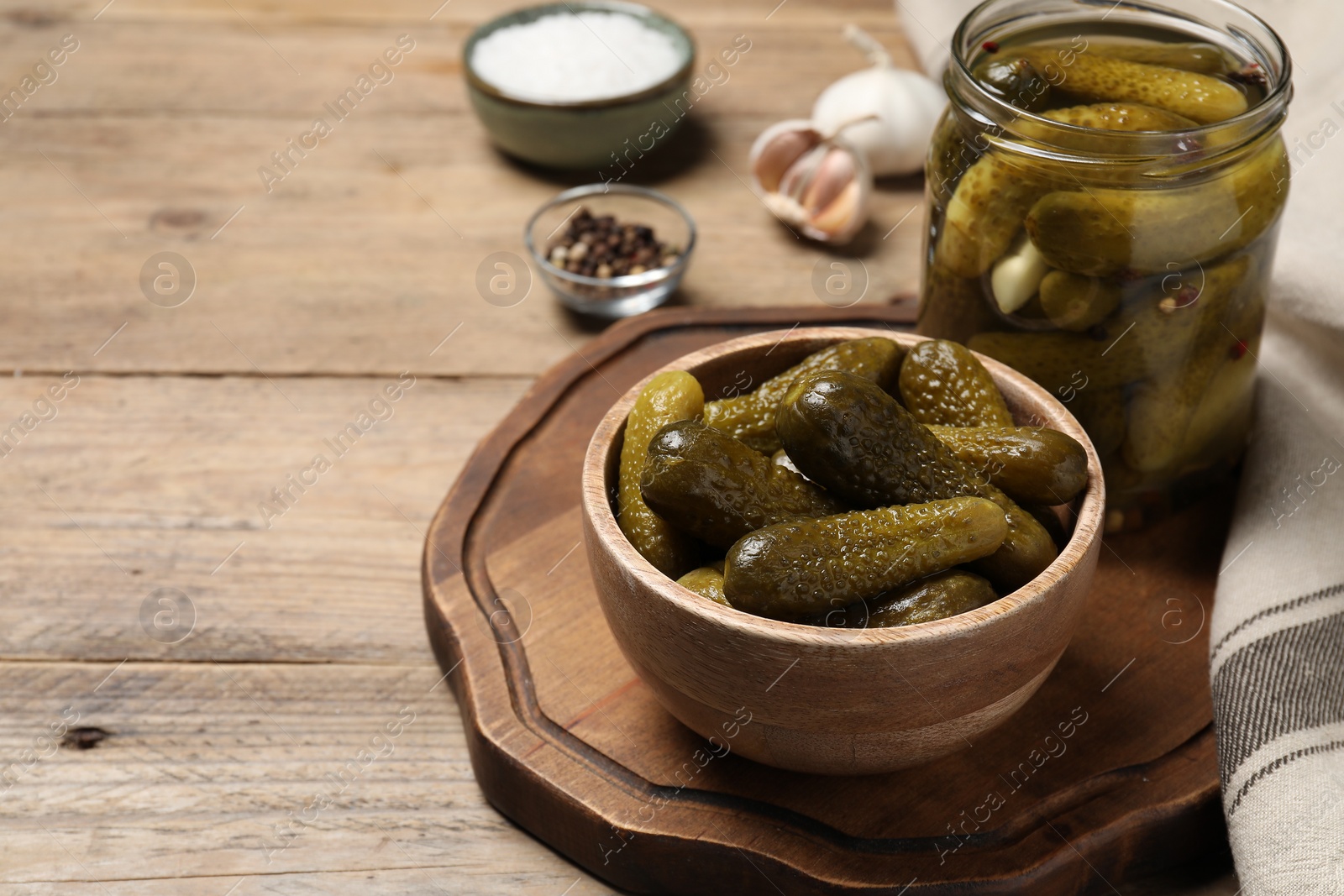 Photo of Tasty pickled cucumbers in jar and bowl on wooden table. Space for text