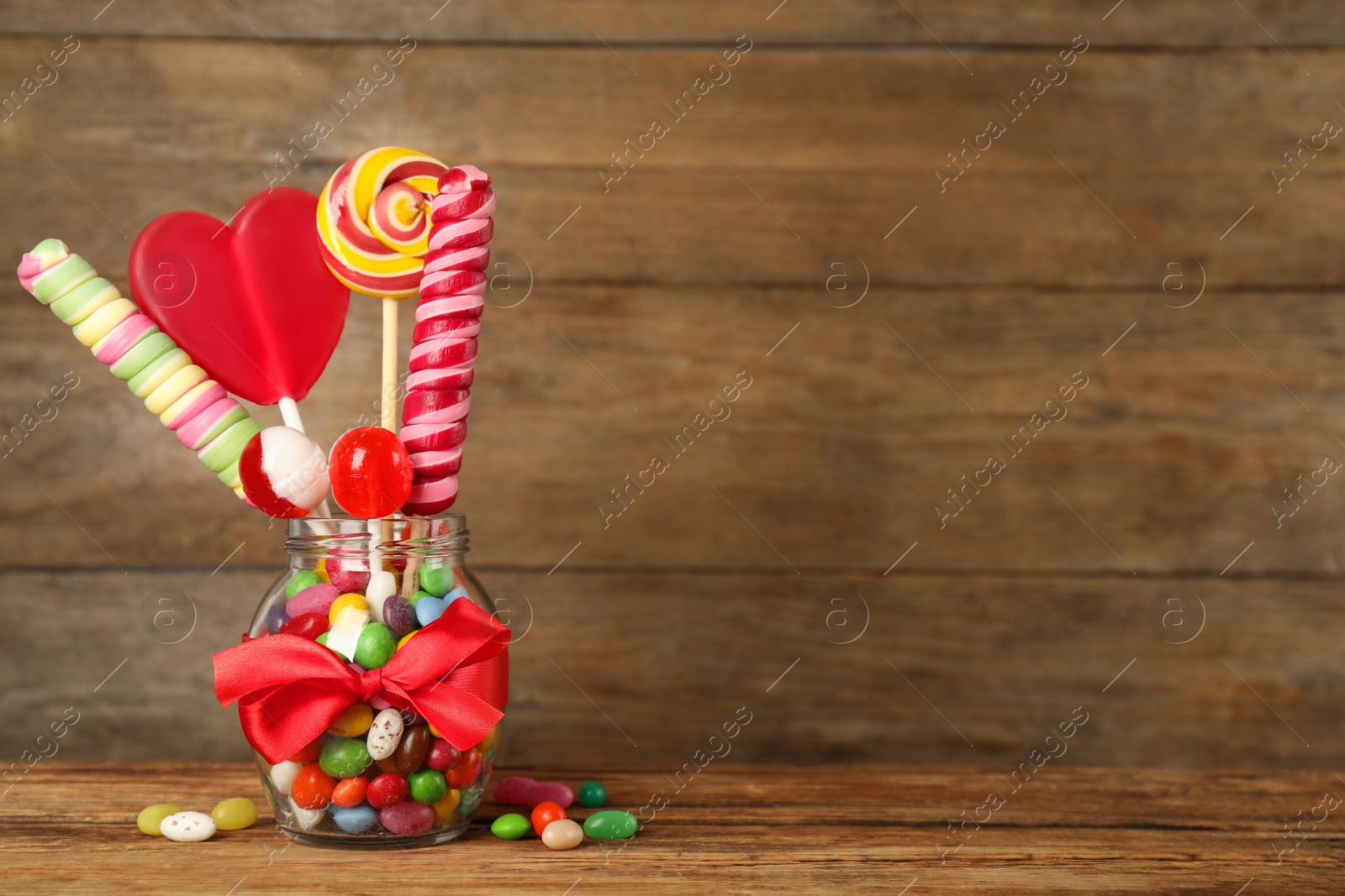 Photo of Jar with different delicious candies on wooden table, space for text