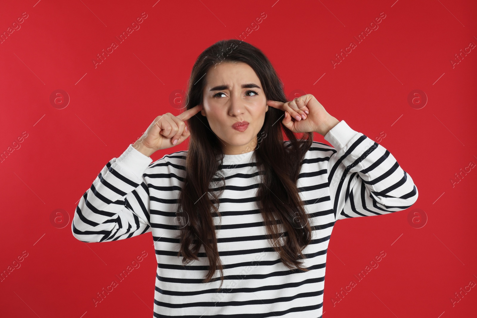 Photo of Emotional young woman covering ears with fingers on red background