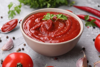 Photo of Organic ketchup in bowl and ingredients on grey textured table, closeup. Tomato sauce