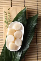 Fresh raw scallops, thyme and green leaves on bamboo mat, flat lay