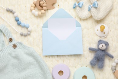 Baby shower party. Envelope surrounded by stuff for child on light knitted fabric, flat lay