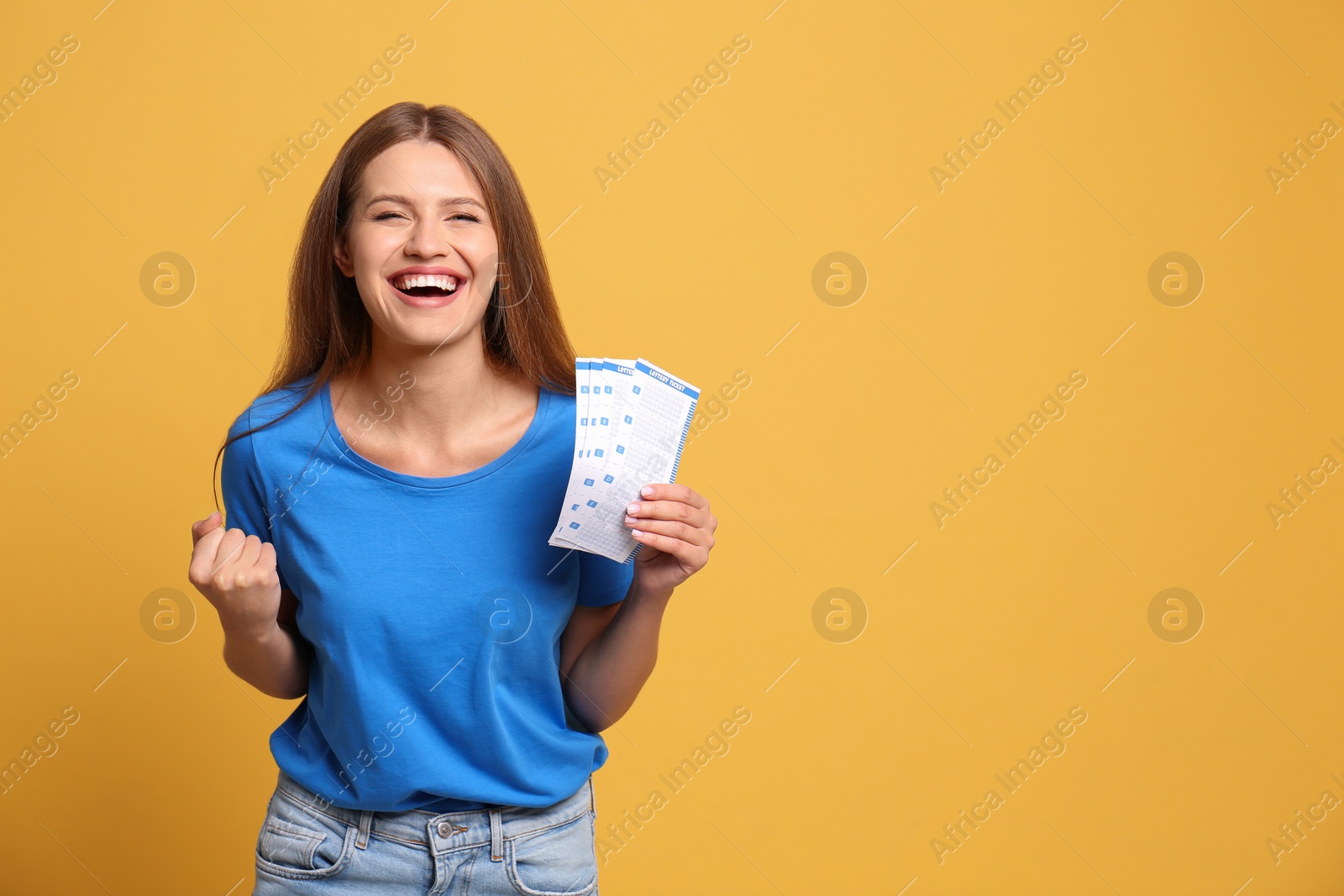 Photo of Portrait of happy young woman with lottery tickets on yellow background, space for text