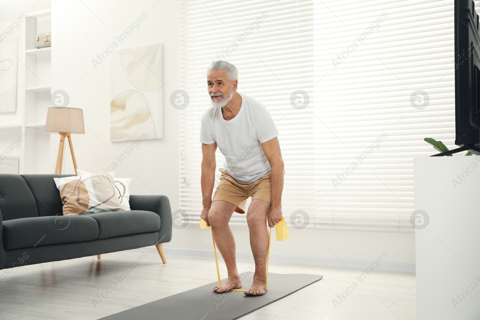 Photo of Senior man doing exercise with fitness elastic band on mat at home