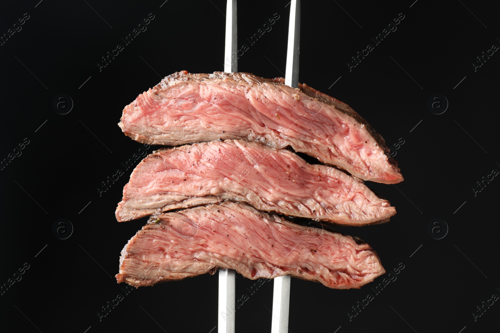 Photo of Meat fork with grilled beef pieces on black background, closeup