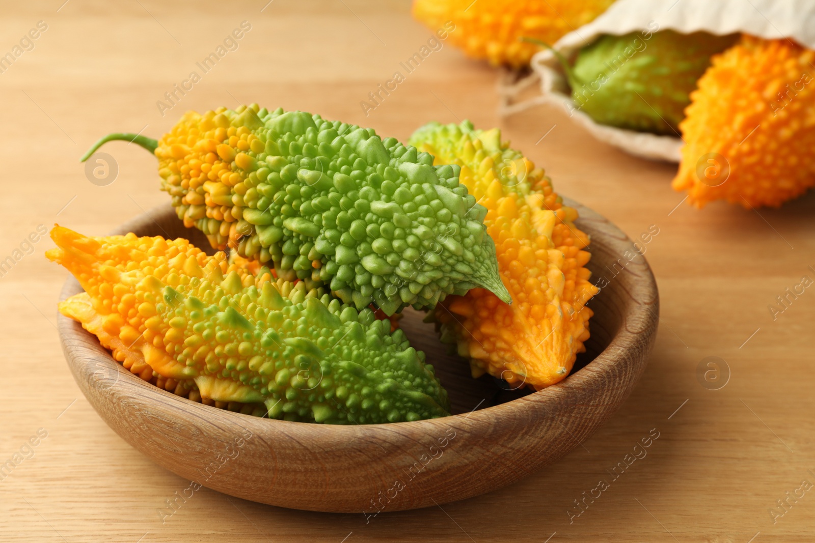 Photo of Bowl with fresh bitter melons on wooden table, closeup