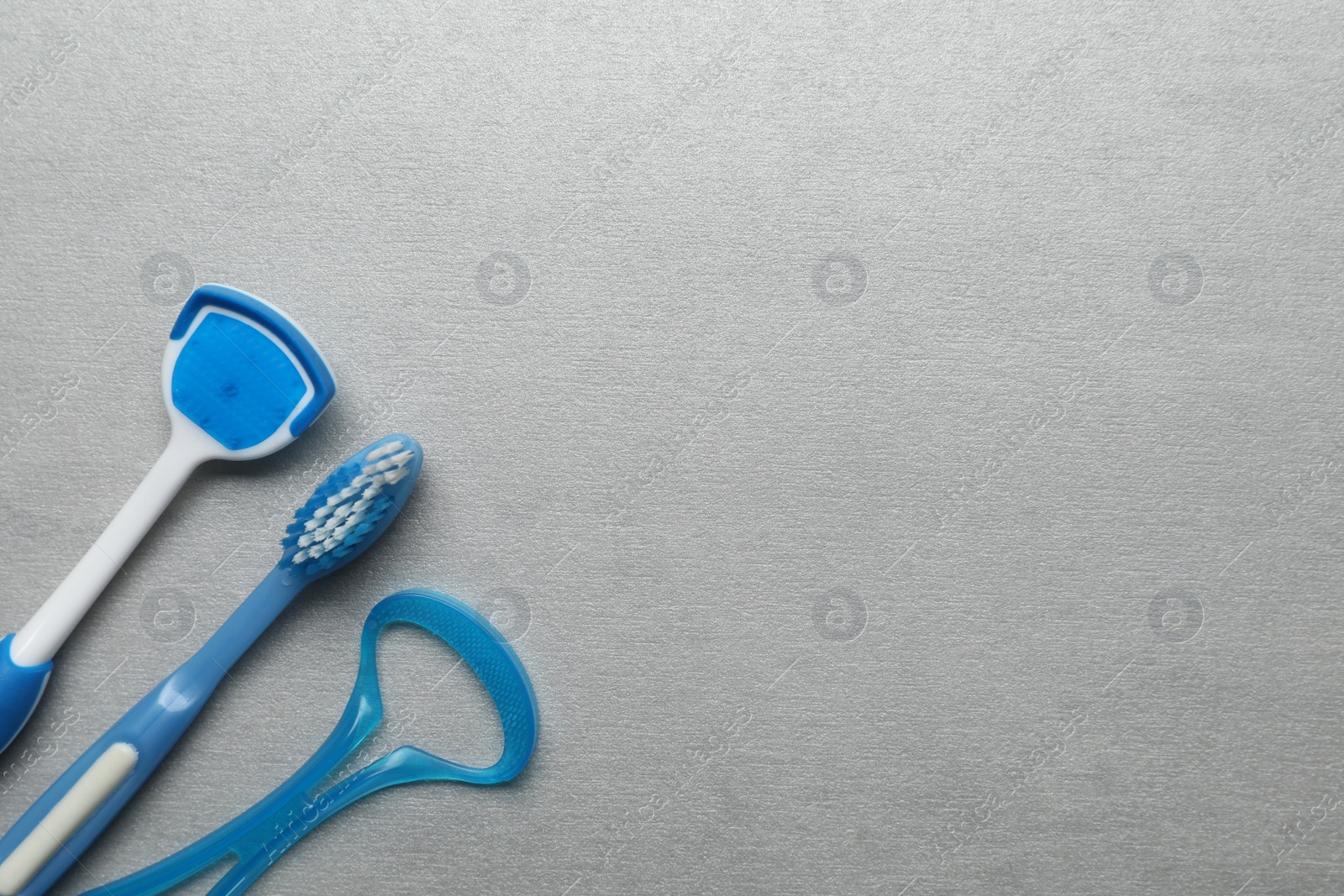 Photo of Tongue cleaners and toothbrush on light grey table, flat lay. Space for text