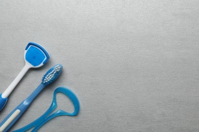 Photo of Tongue cleaners and toothbrush on light grey table, flat lay. Space for text