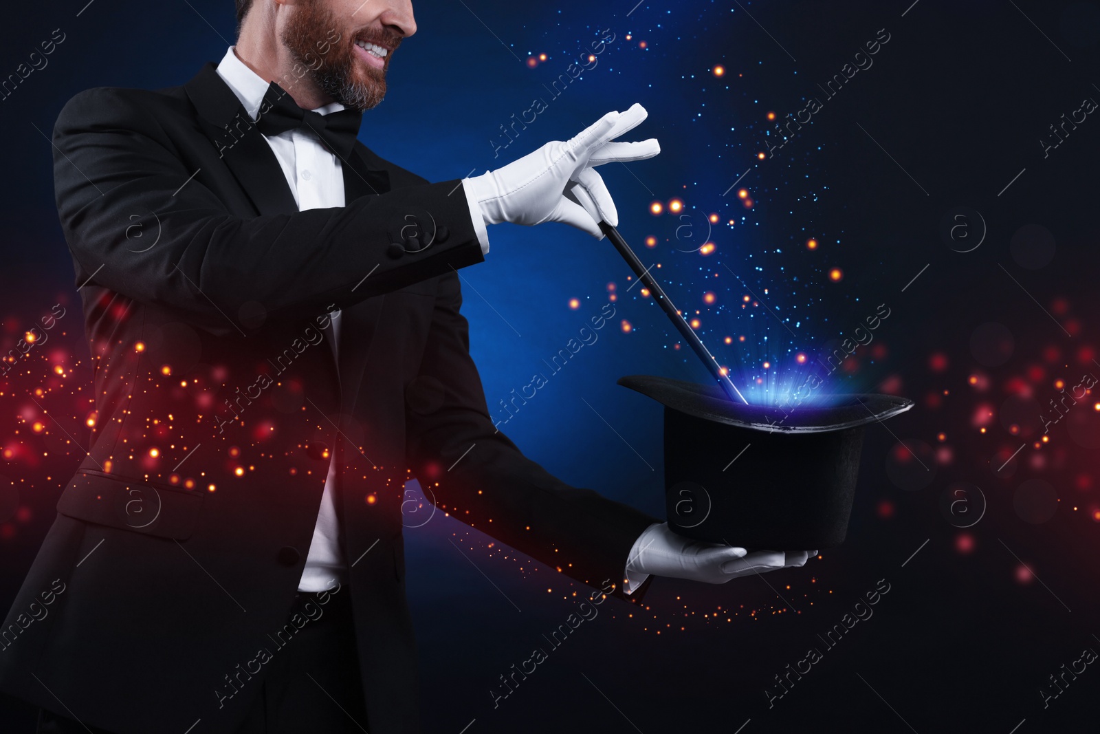 Image of Smiling magician showing trick with wand and top hat on dark blue background, closeup