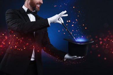 Image of Smiling magician showing trick with wand and top hat on dark blue background, closeup