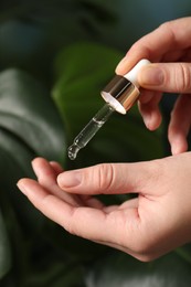 Photo of Woman applying cosmetic serum onto hand on blurred background, closeup