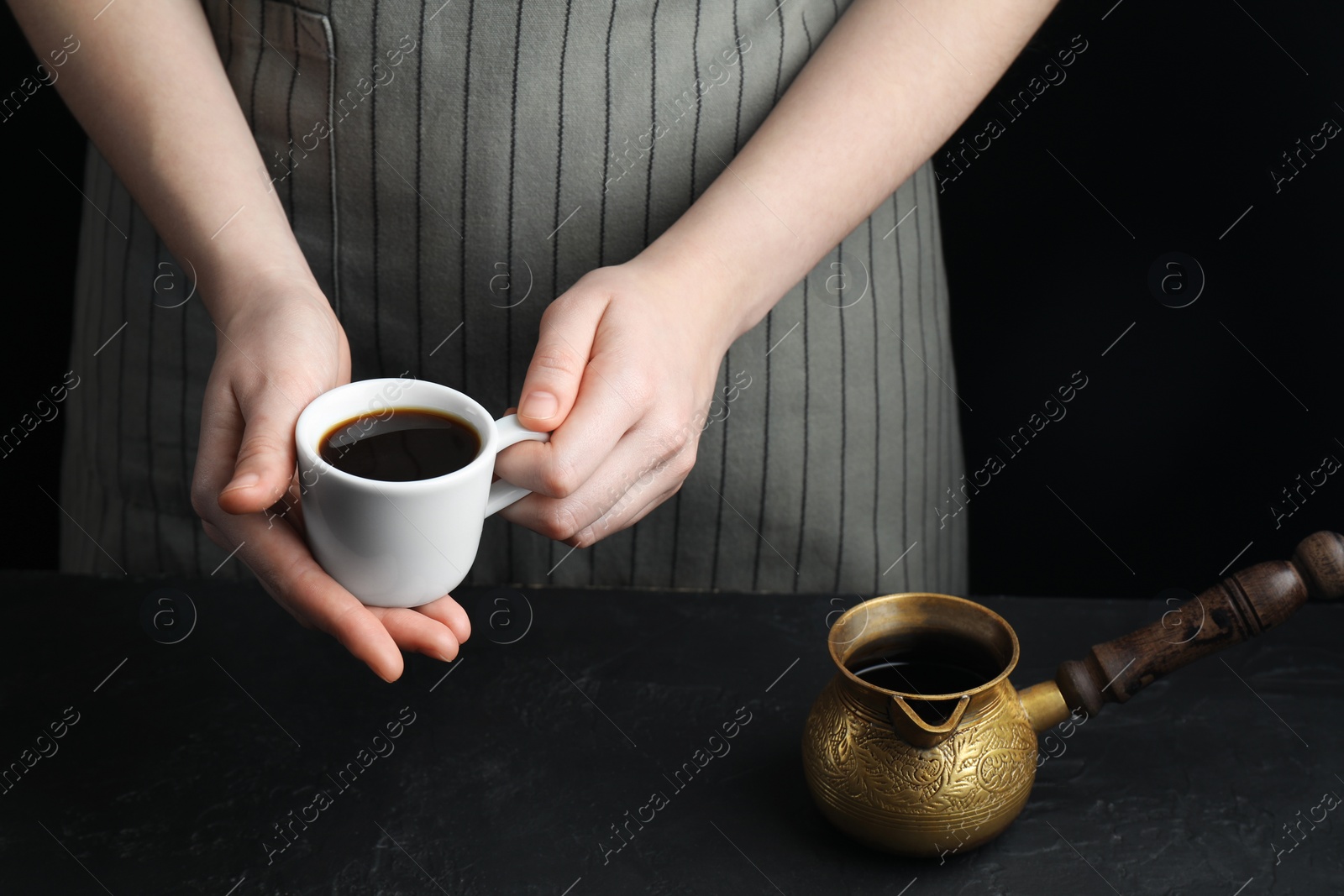 Photo of Turkish coffee. Woman with cup of freshly brewed beverage and cezve at black table, closeup