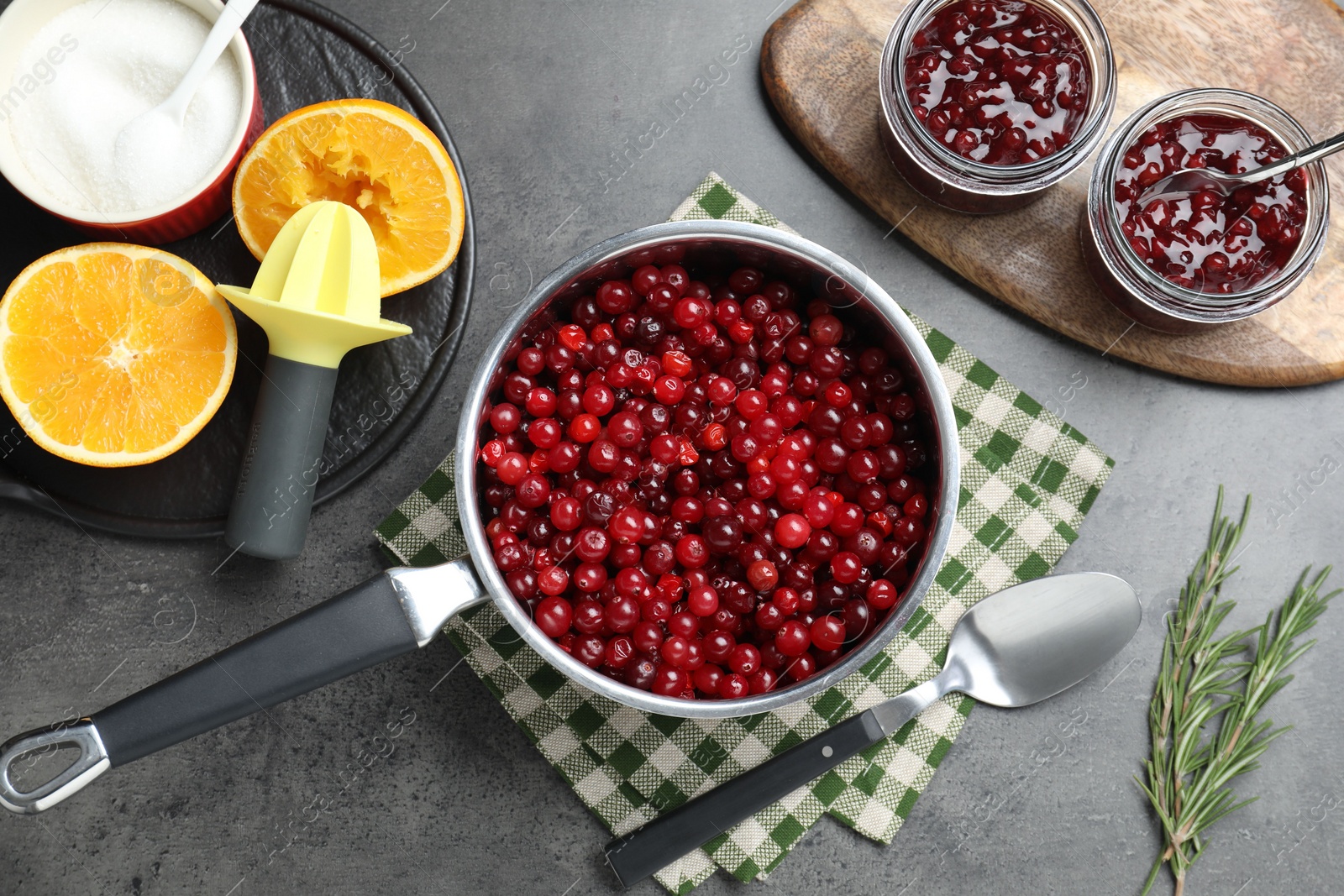 Photo of Making cranberry sauce. Fresh cranberries in saucepan and ingredients on gray table, flat lay