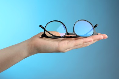 Photo of Woman holding glasses with black frame on light blue background, closeup