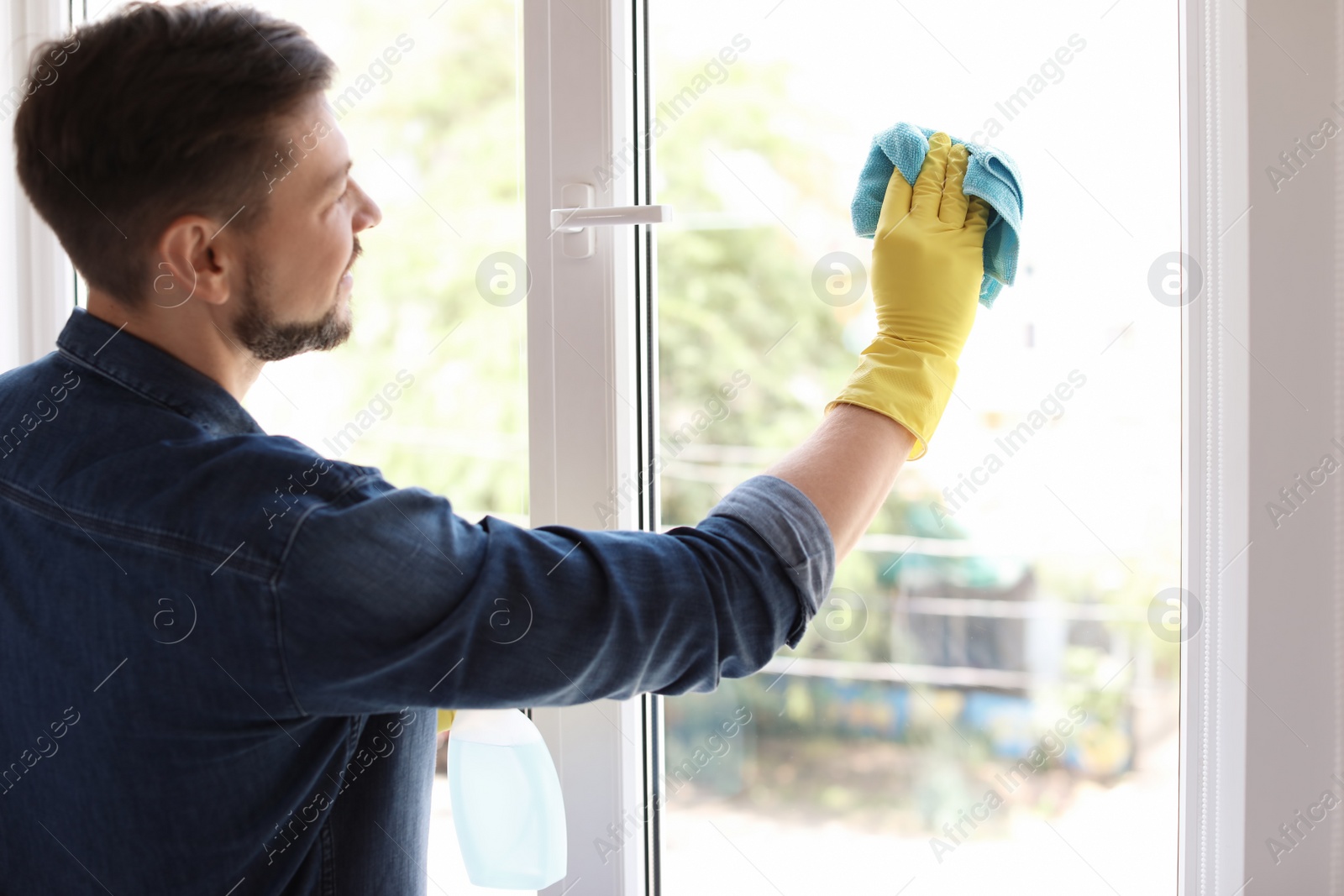 Photo of Man in casual clothes washing window glass at home