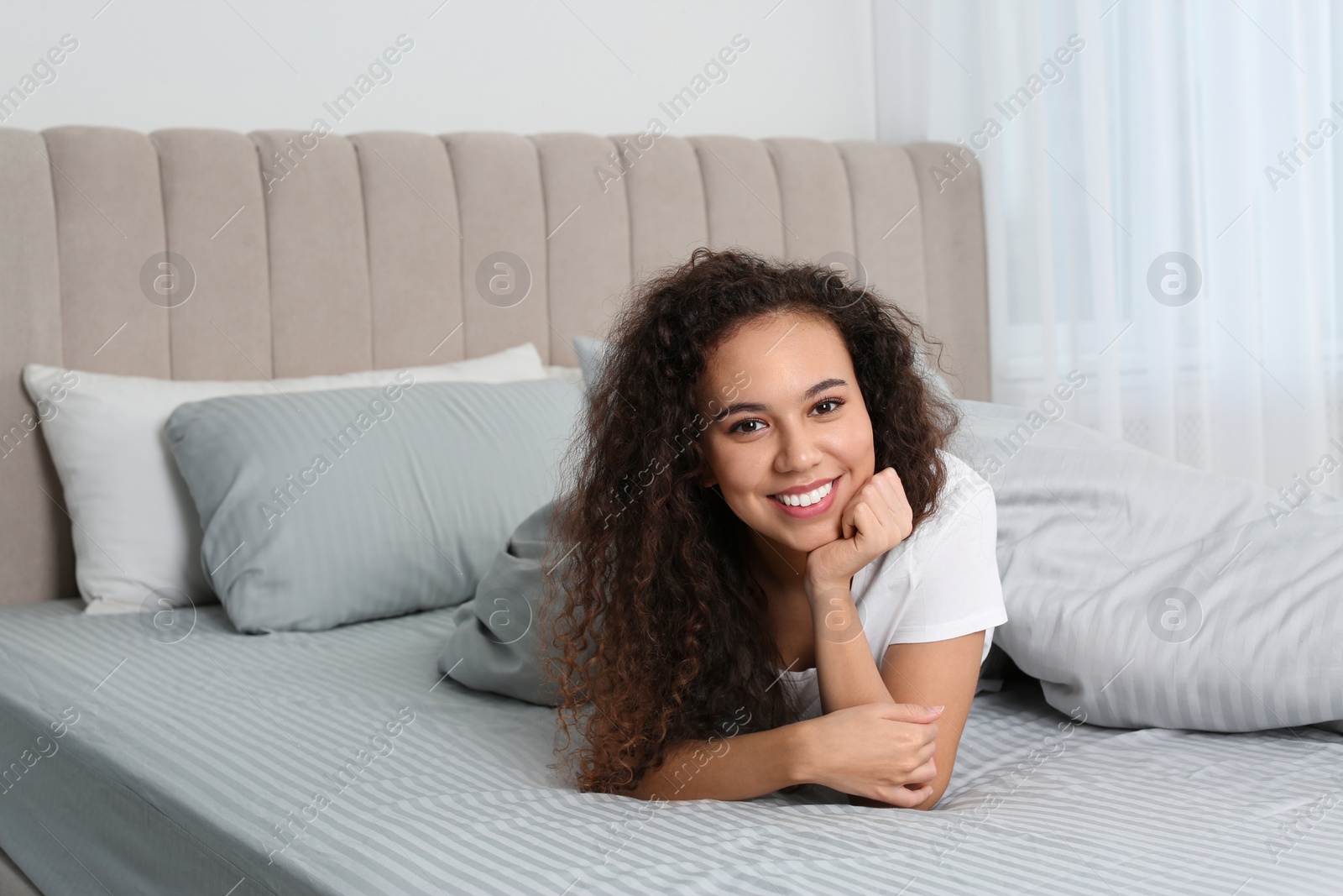 Photo of Happy beautiful African American woman lying on bed at home