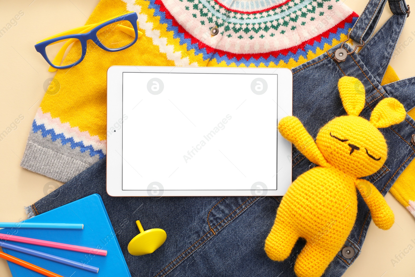 Photo of Modern tablet, clothes, stationery and toy bunny on beige background, flat lay. Space for text