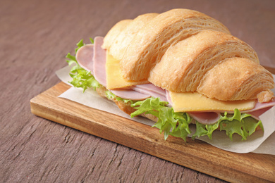 Photo of Tasty croissant sandwich with ham on brown table, closeup