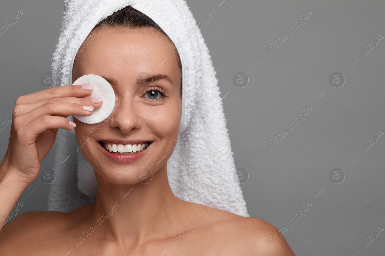 Photo of Smiling woman removing makeup with cotton pad on grey background, closeup. Space for text