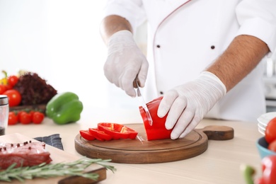 Professional chef cutting pepper on table in kitchen, closeup