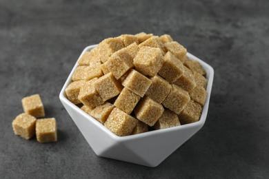 Photo of Brown sugar cubes in bowl on grey table