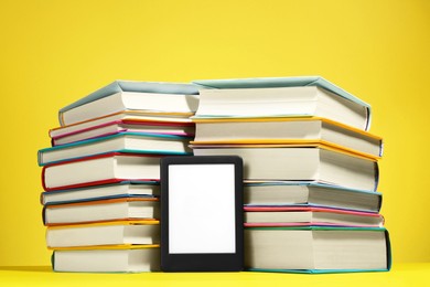 Photo of Modern e-book reader and stacks of hard cover books on yellow background
