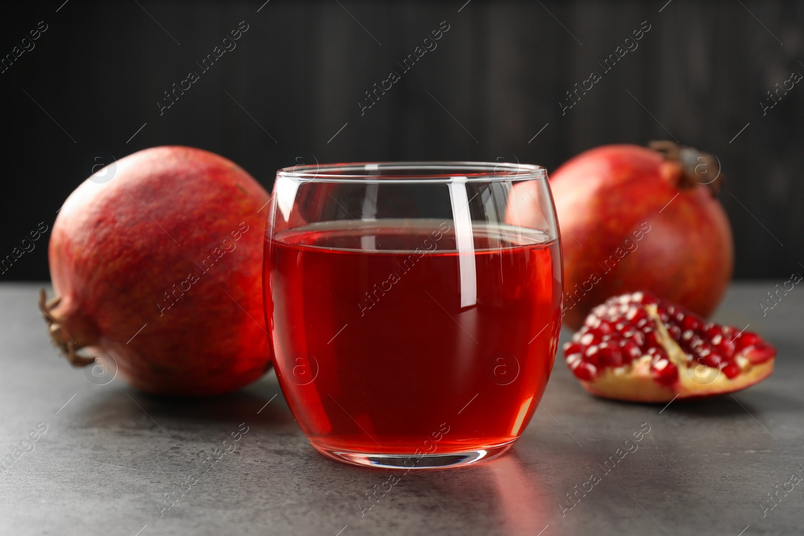Photo of Tasty pomegranate juice in glass and fresh fruit on grey table