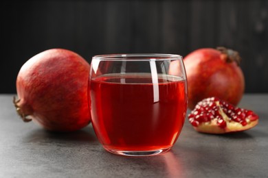 Photo of Tasty pomegranate juice in glass and fresh fruit on grey table