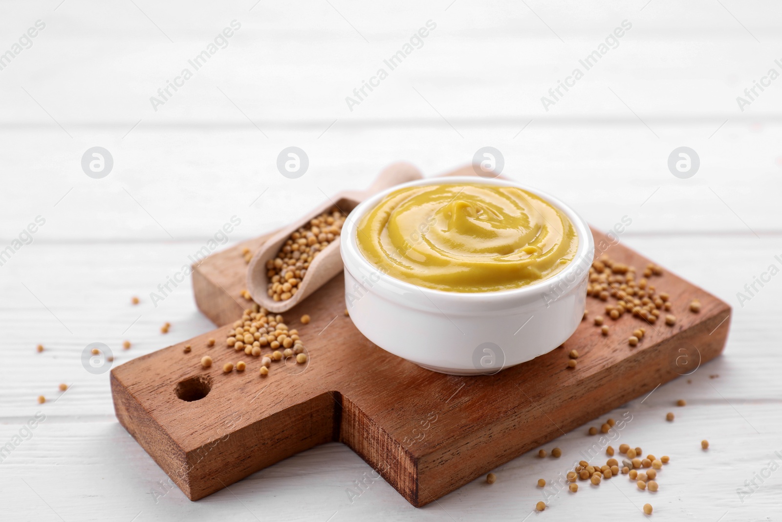 Photo of Bowl with delicious mustard and seeds on white wooden table