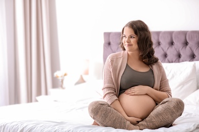 Photo of Young pregnant woman sitting on bed at home