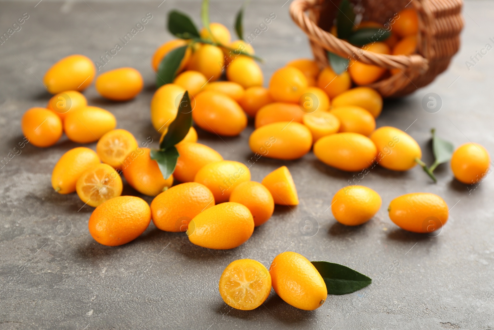 Photo of Fresh ripe kumquats and leaves on grey table