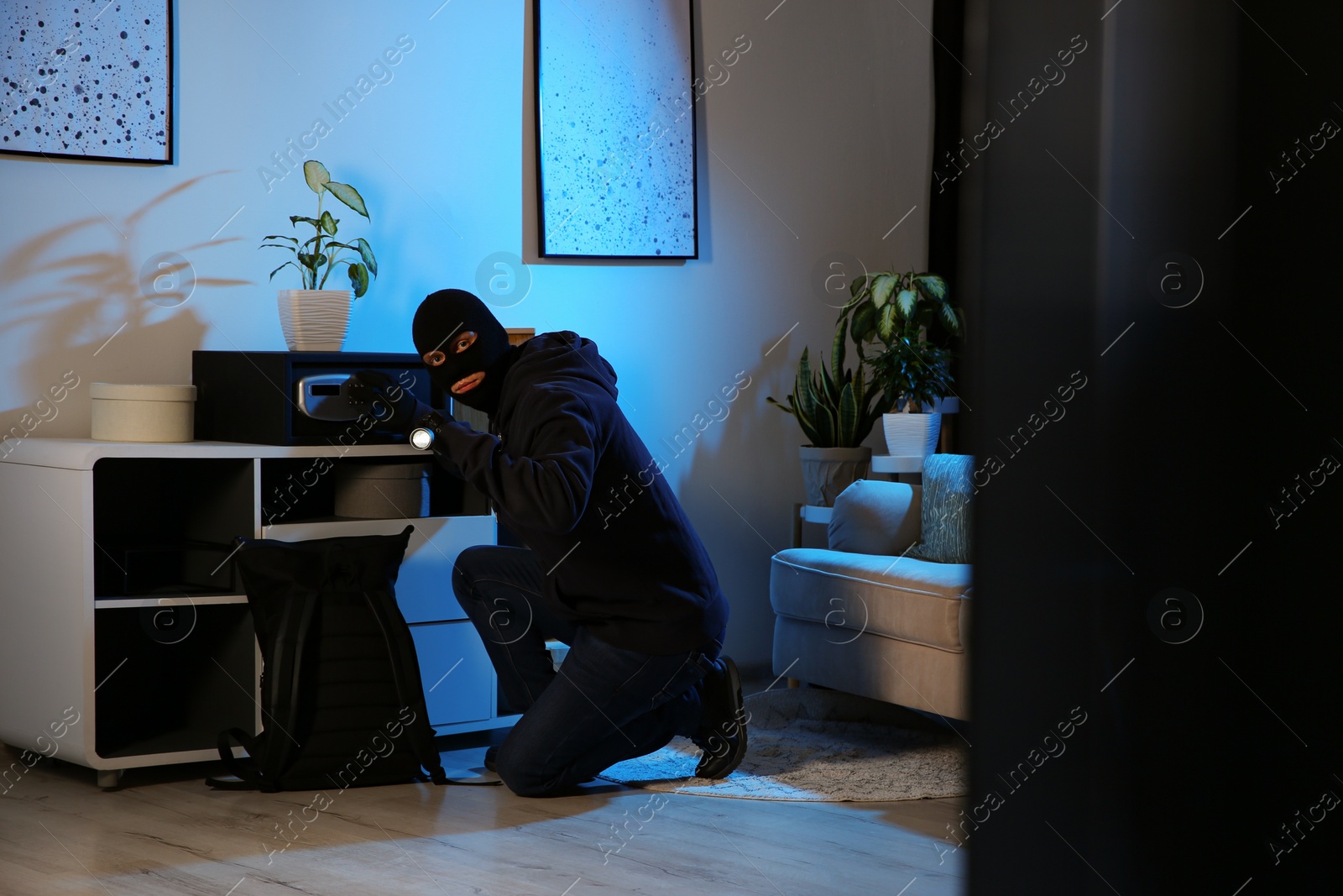 Photo of Thief with flashlight near steel safe indoors at night