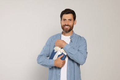 Handsome man holding gift box on light grey background