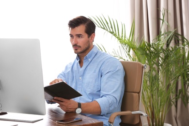 Handsome young man working with notebook and computer at table in office