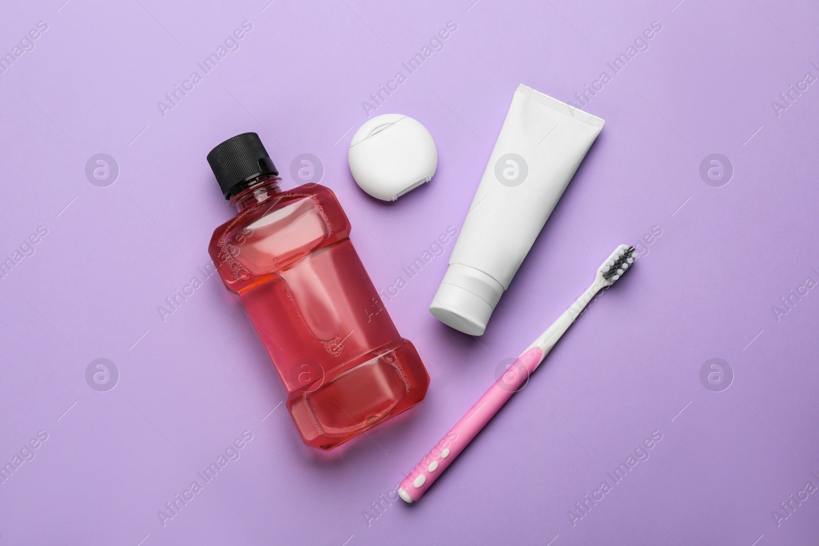 Photo of Mouthwash, toothbrush, paste and dental floss on violet background, flat lay