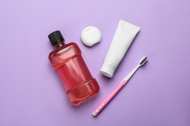 Photo of Mouthwash, toothbrush, paste and dental floss on violet background, flat lay
