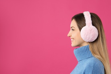 Happy woman wearing warm earmuffs on pink background, space for text