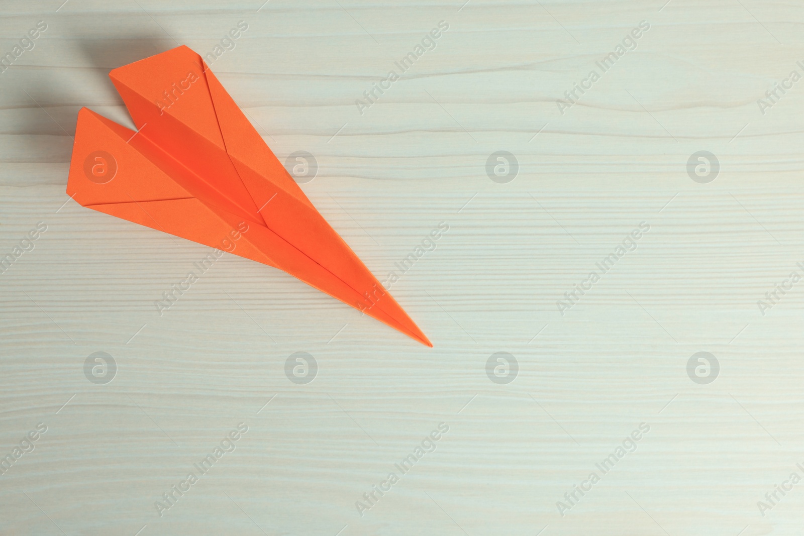 Photo of Handmade orange paper plane on beige wooden table, top view. Space for text