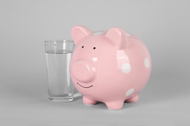 Water scarcity concept. Piggy bank and glass of drink on grey background