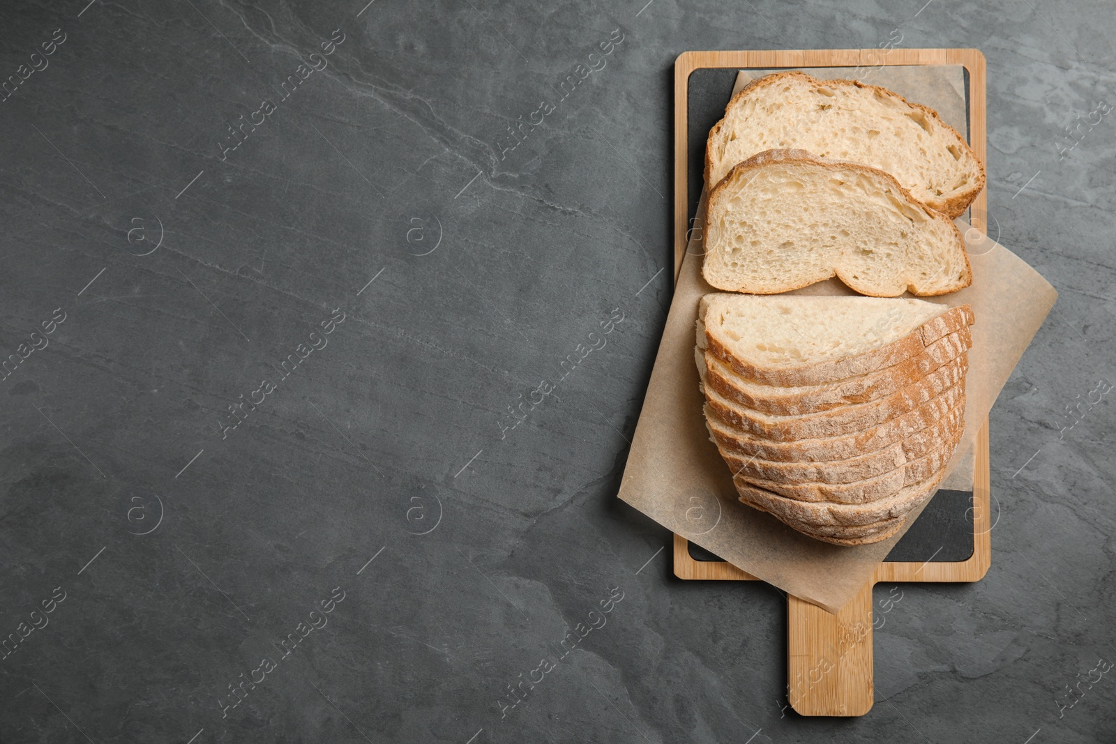 Photo of Board with cut bread on grey table, top view. Space for text