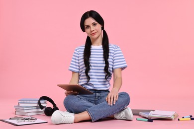 Photo of Student with tablet sitting among books and stationery on pink background