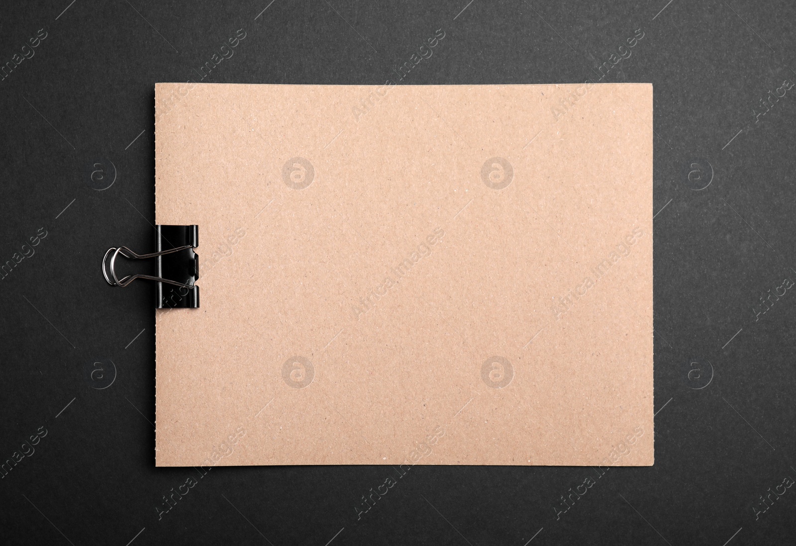 Photo of Sheet of brown paper with clip on black background, top view