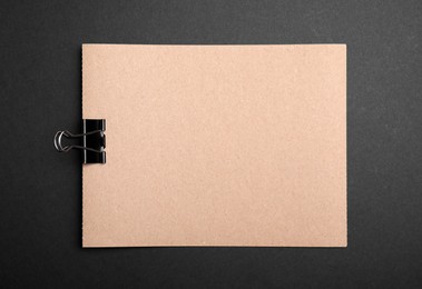 Sheet of brown paper with clip on black background, top view