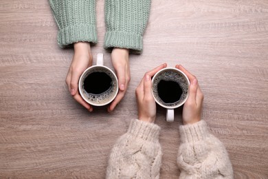 Women with cups of coffee at wooden table, top view