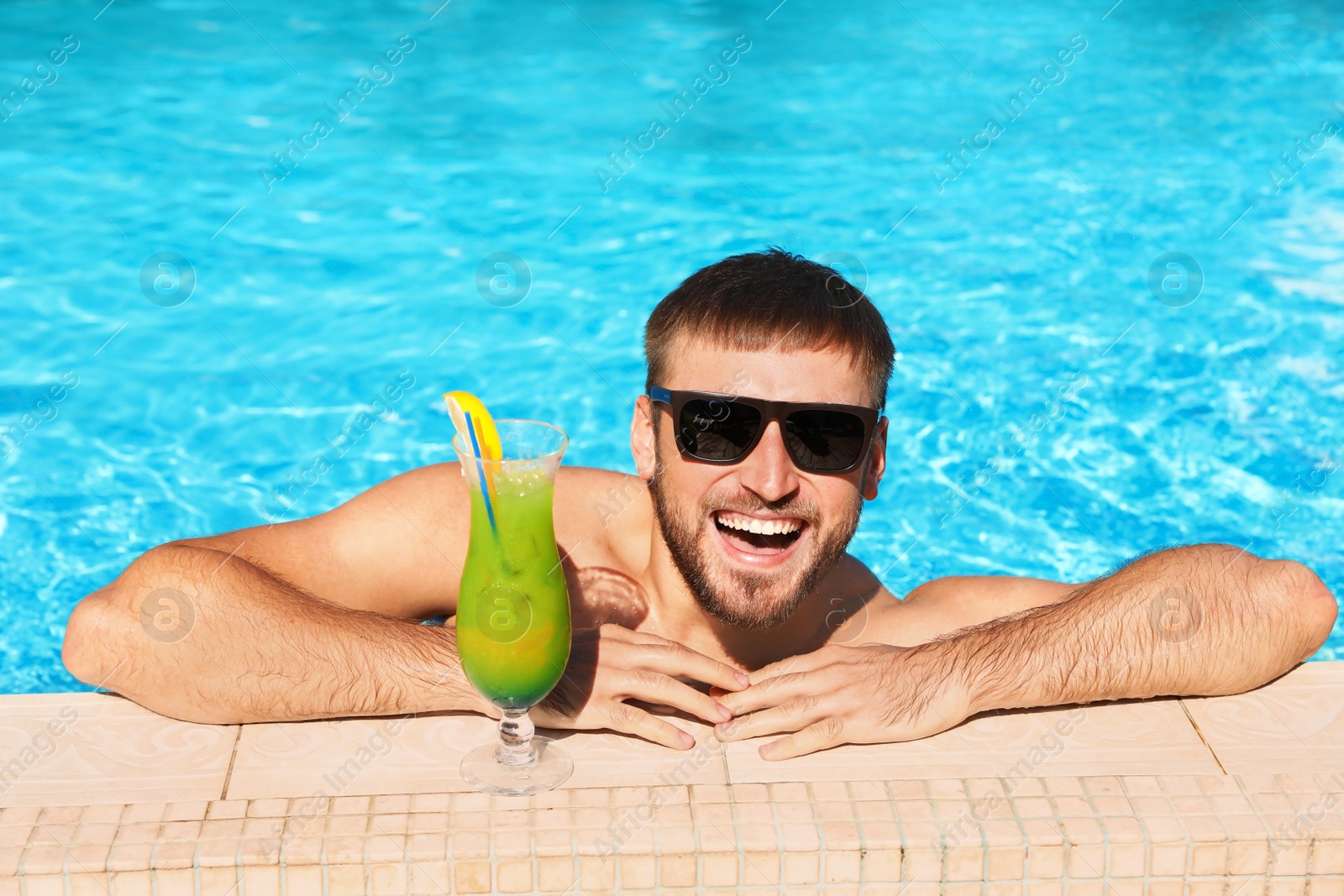 Photo of Young bearded man with refreshing cocktail in swimming pool at resort