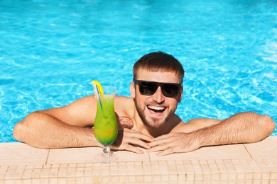 Young bearded man with refreshing cocktail in swimming pool at resort