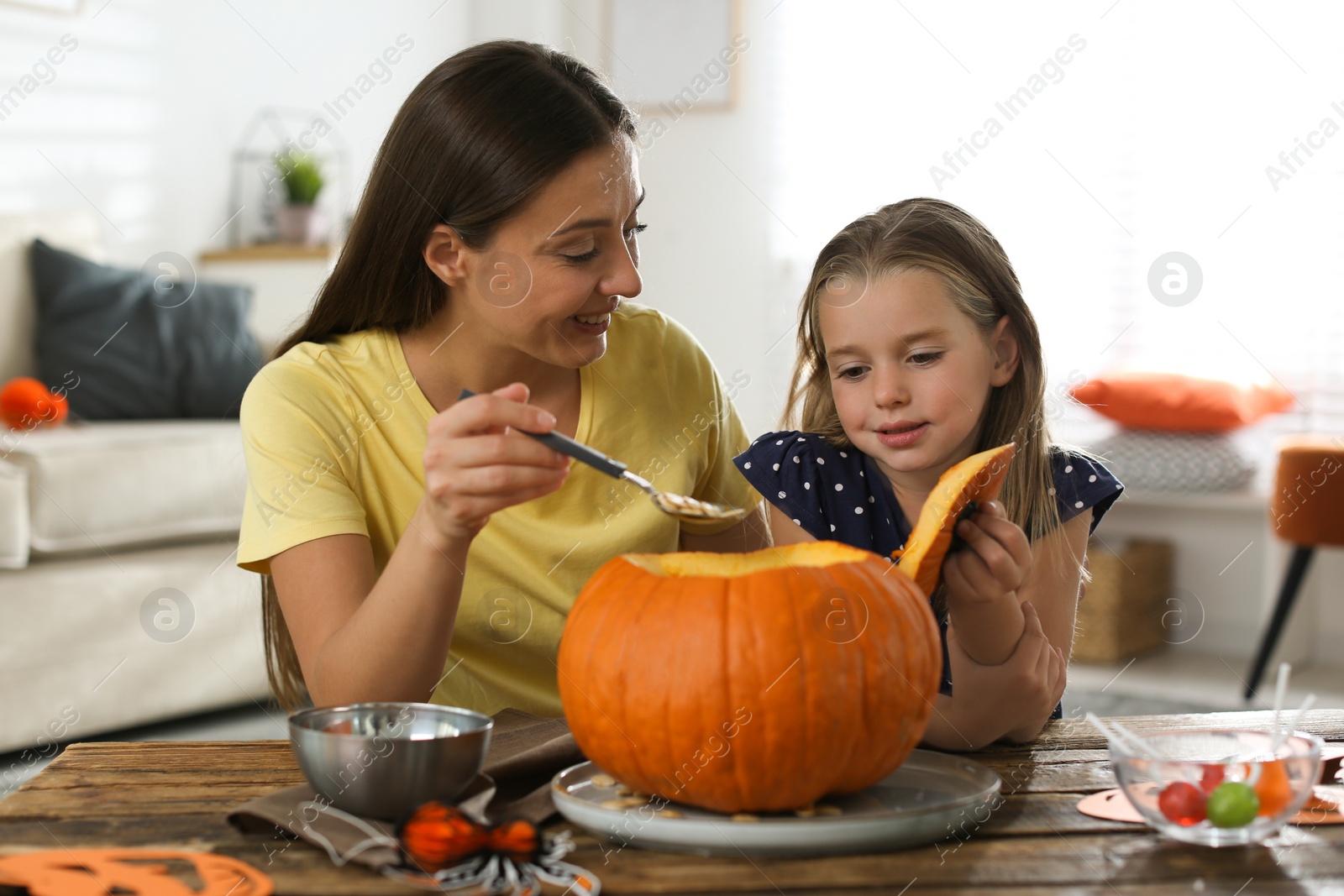Photo of Mother and daughter making pumpkin jack o'lantern at table indoors. Halloween celebration